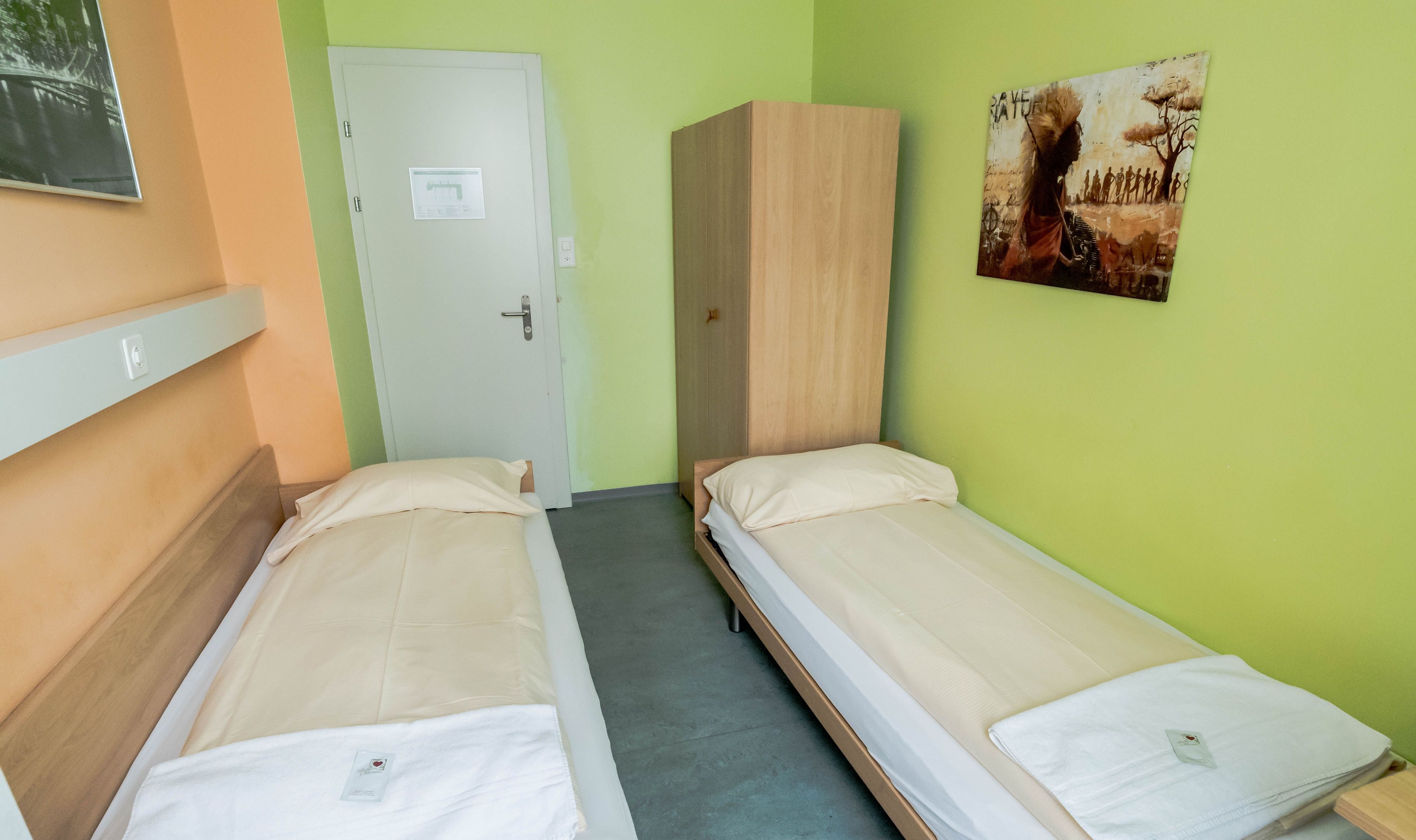 Una habitación con dos camas individuales, un armario, una puerta y un cuadro en la pared.