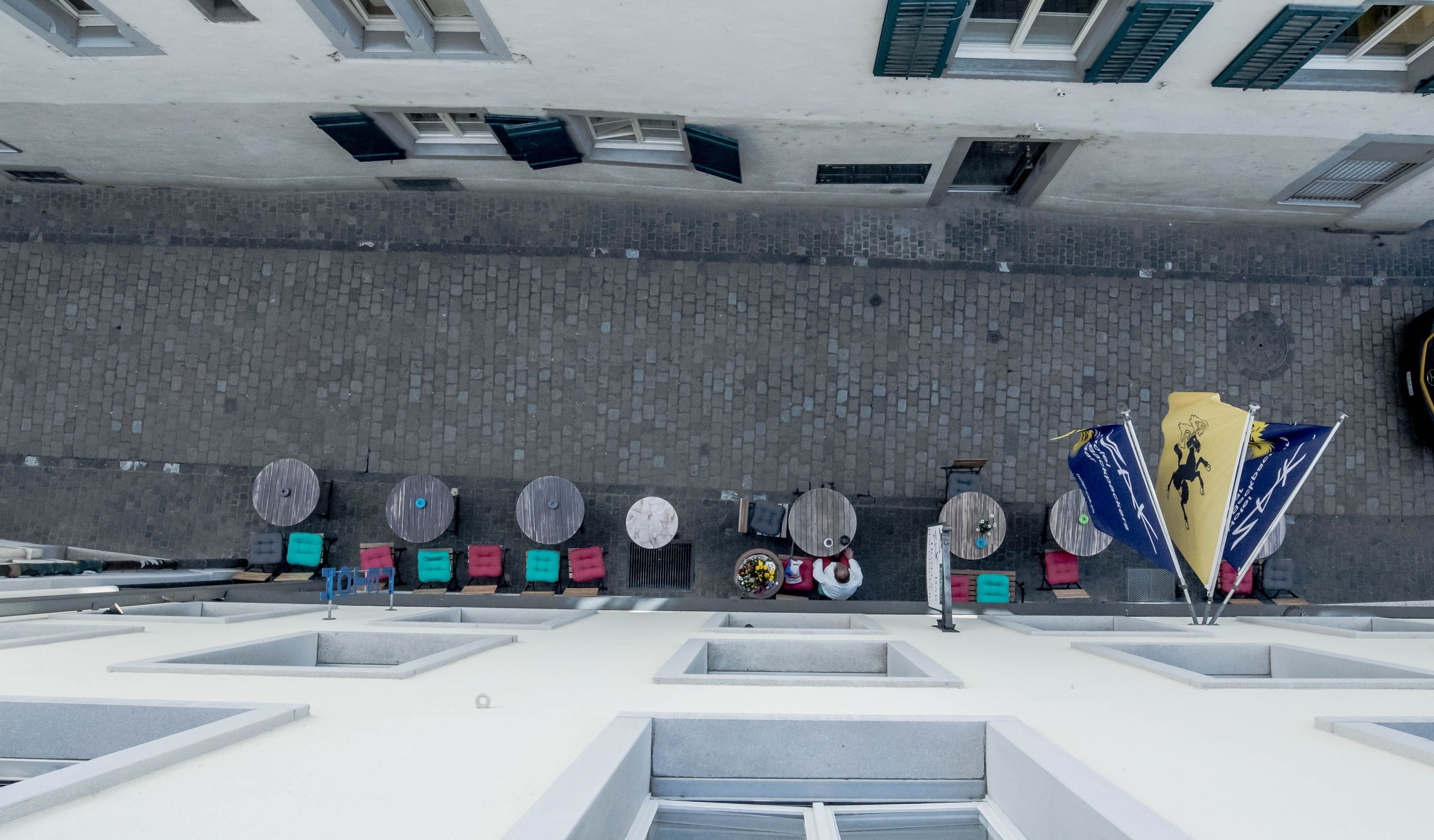 A rooftop terrace with multiple round tables and chairs, a brick wall, and a flag.
