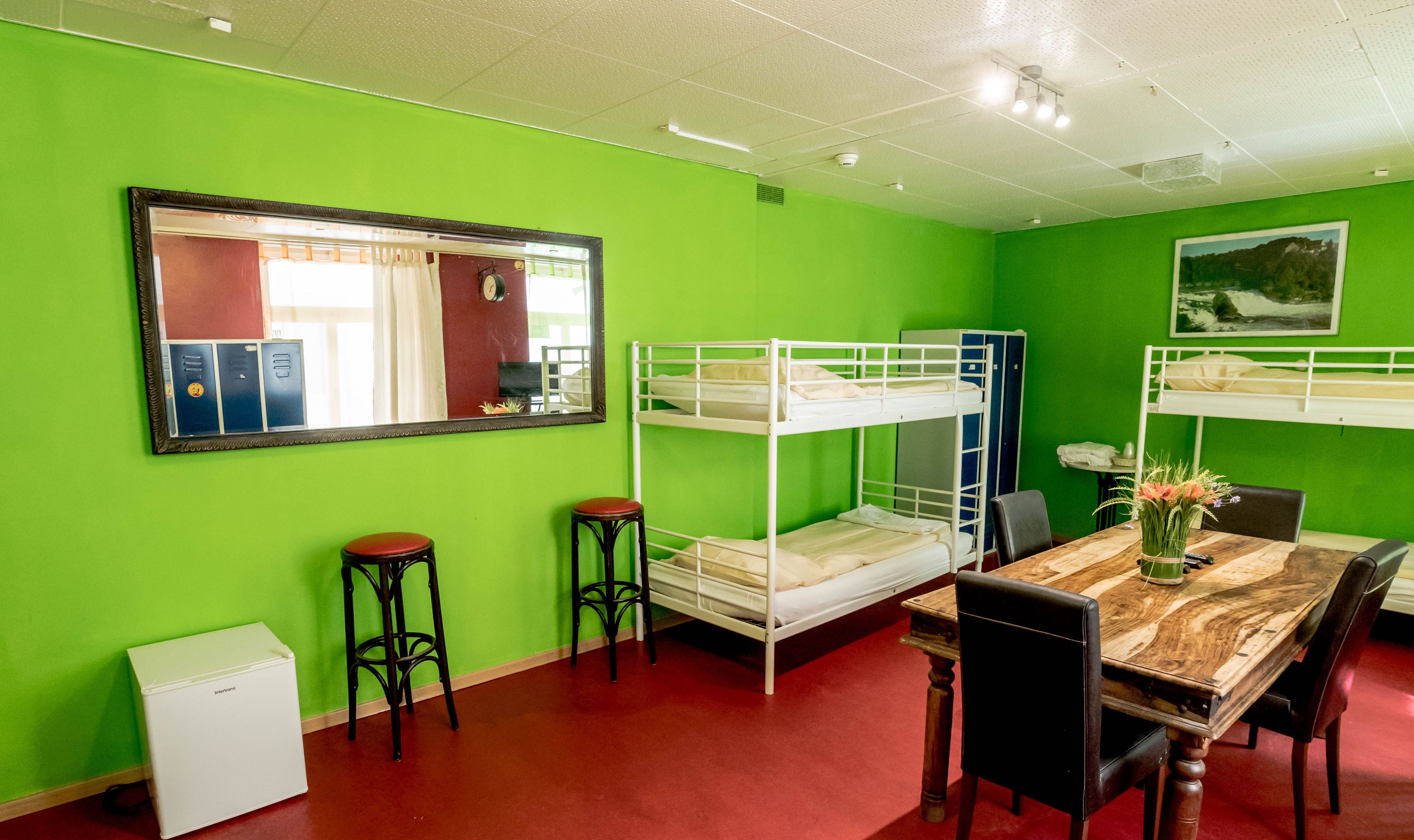 A room with bunk beds, a small table with chairs, a mirror, and a small white appliance.