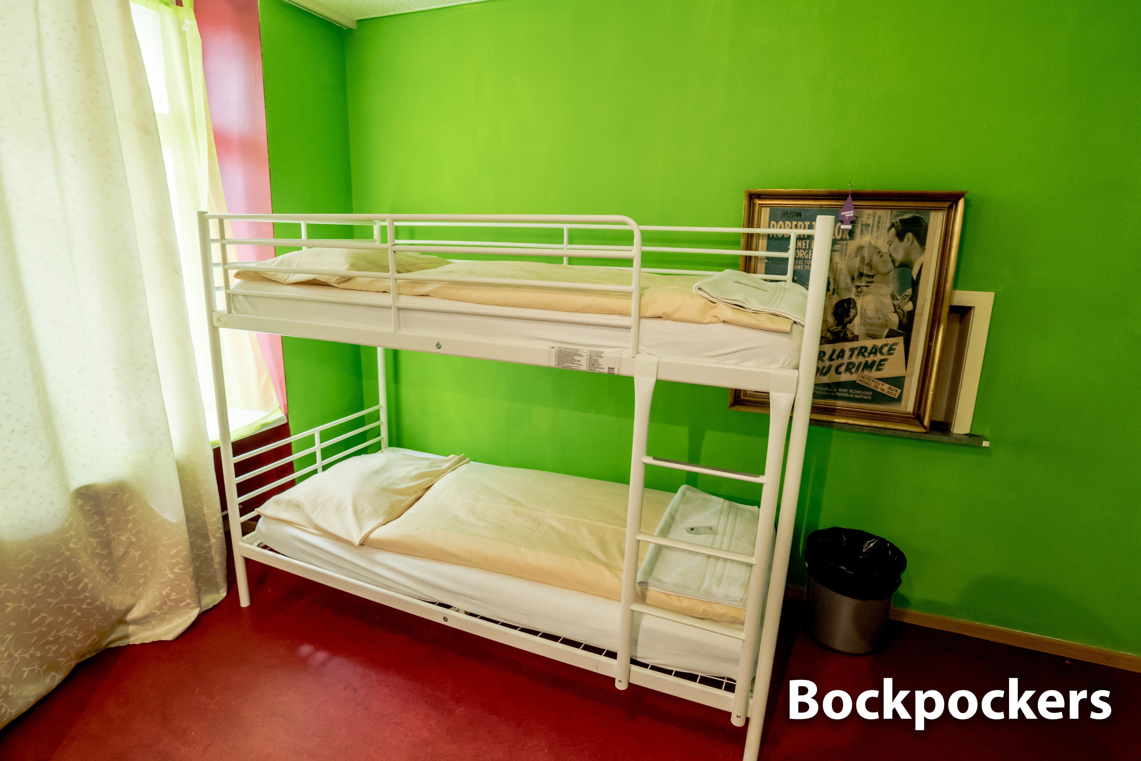 A bunk bed room with green walls, a framed picture on the wall, and a trash can.