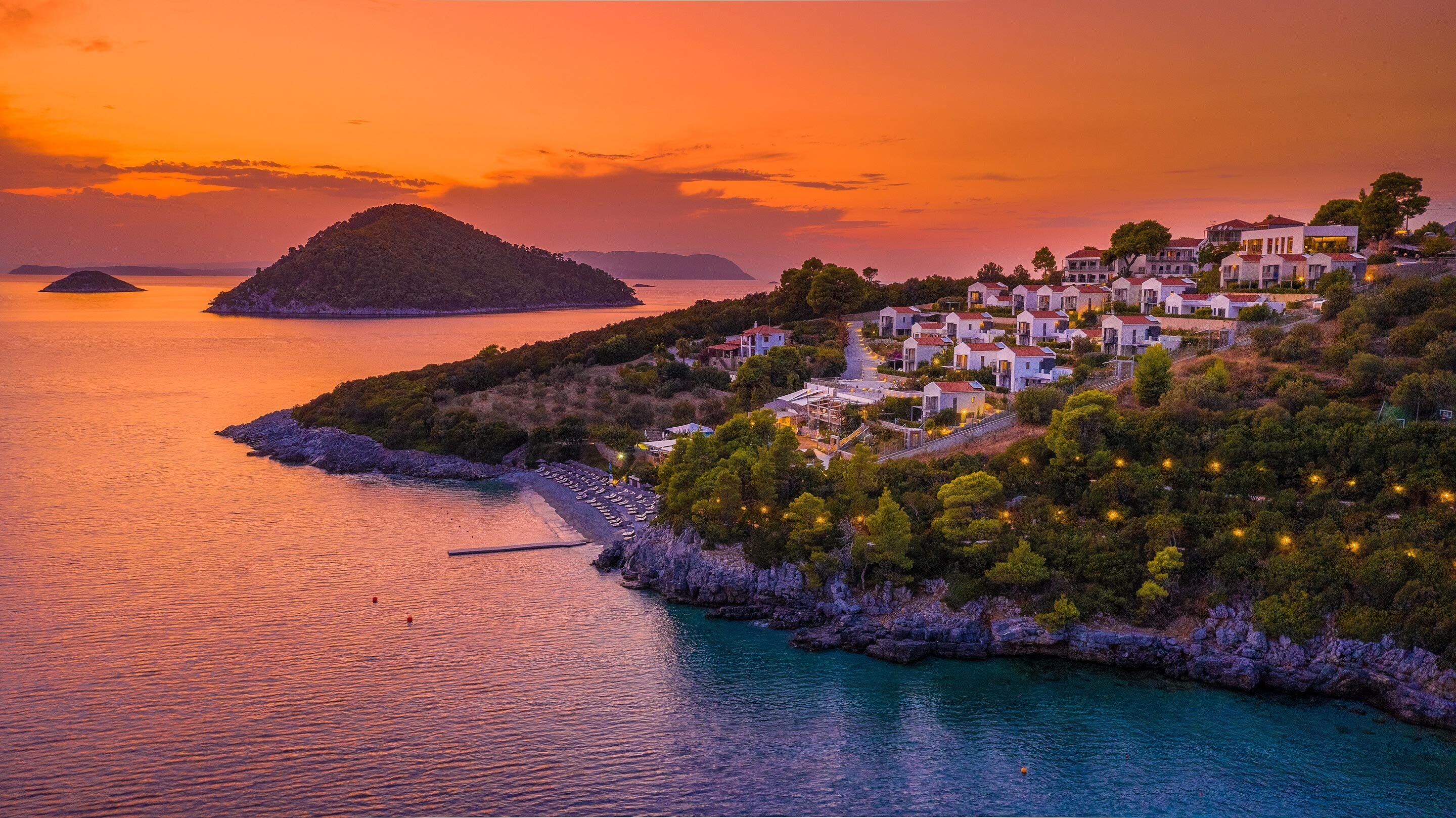 A coastal village with white buildings, a rocky shoreline, and a sunset over the sea.
