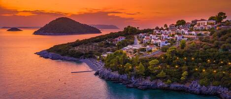A coastal village with white buildings, a rocky shoreline, and a sunset over the sea.