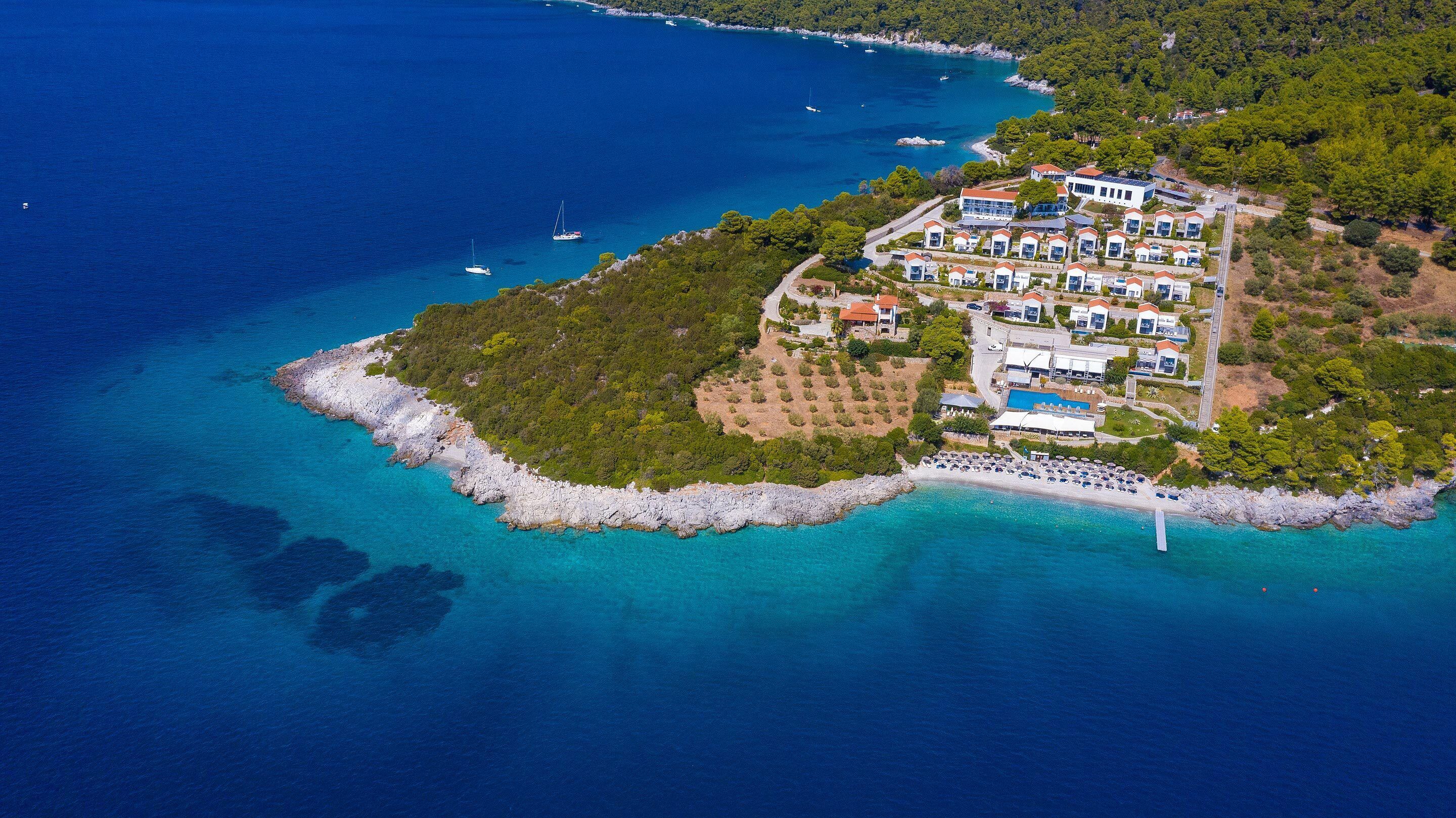 Eine Luftaufnahme eines Küstenresorts mit mehreren Gebäuden, einem Schwimmbecken und einer felsigen Küstenlinie.