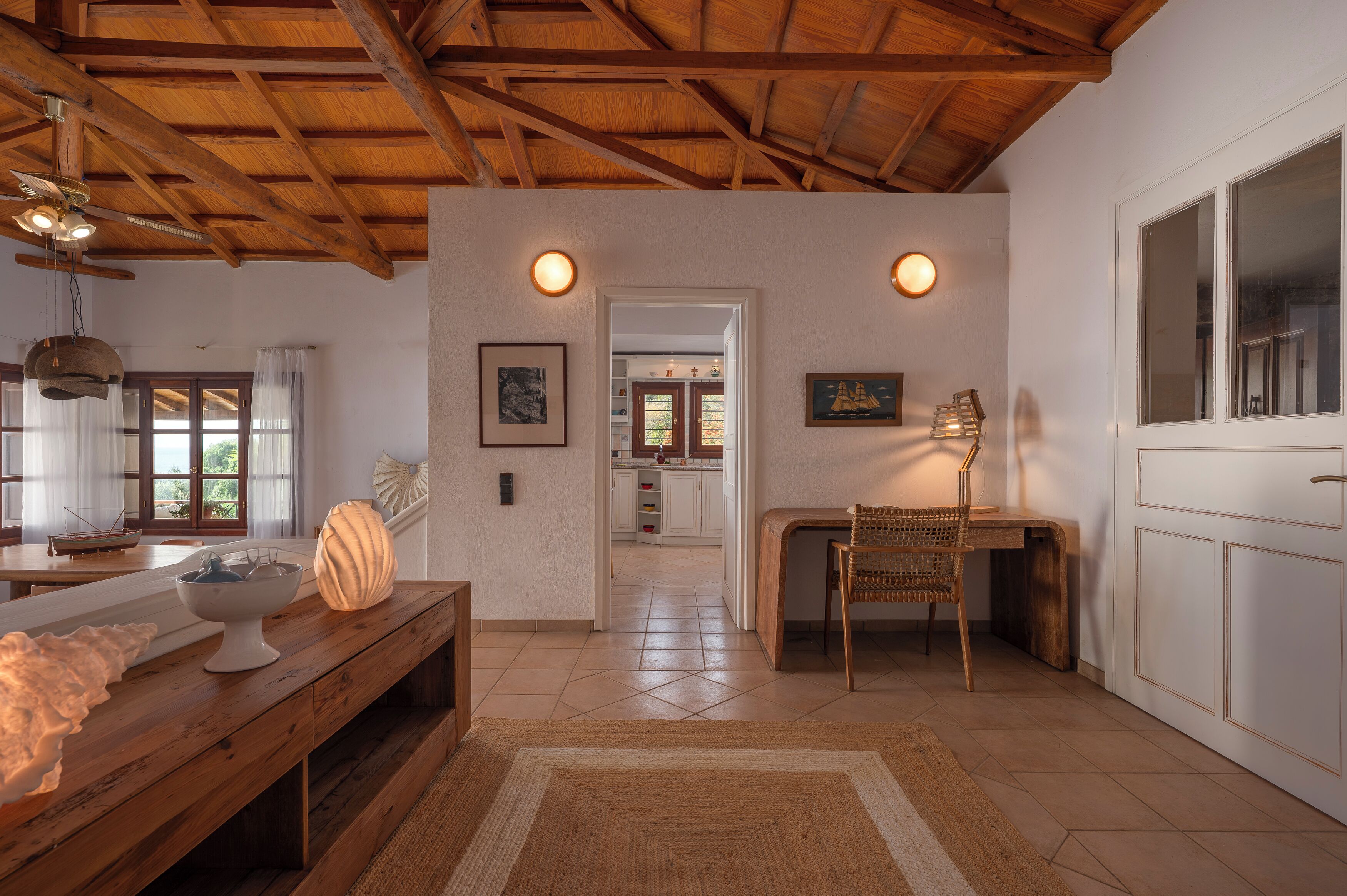 A spacious kitchen with wooden beams, a dining area with a table and chairs, and a view into the adjacent room.