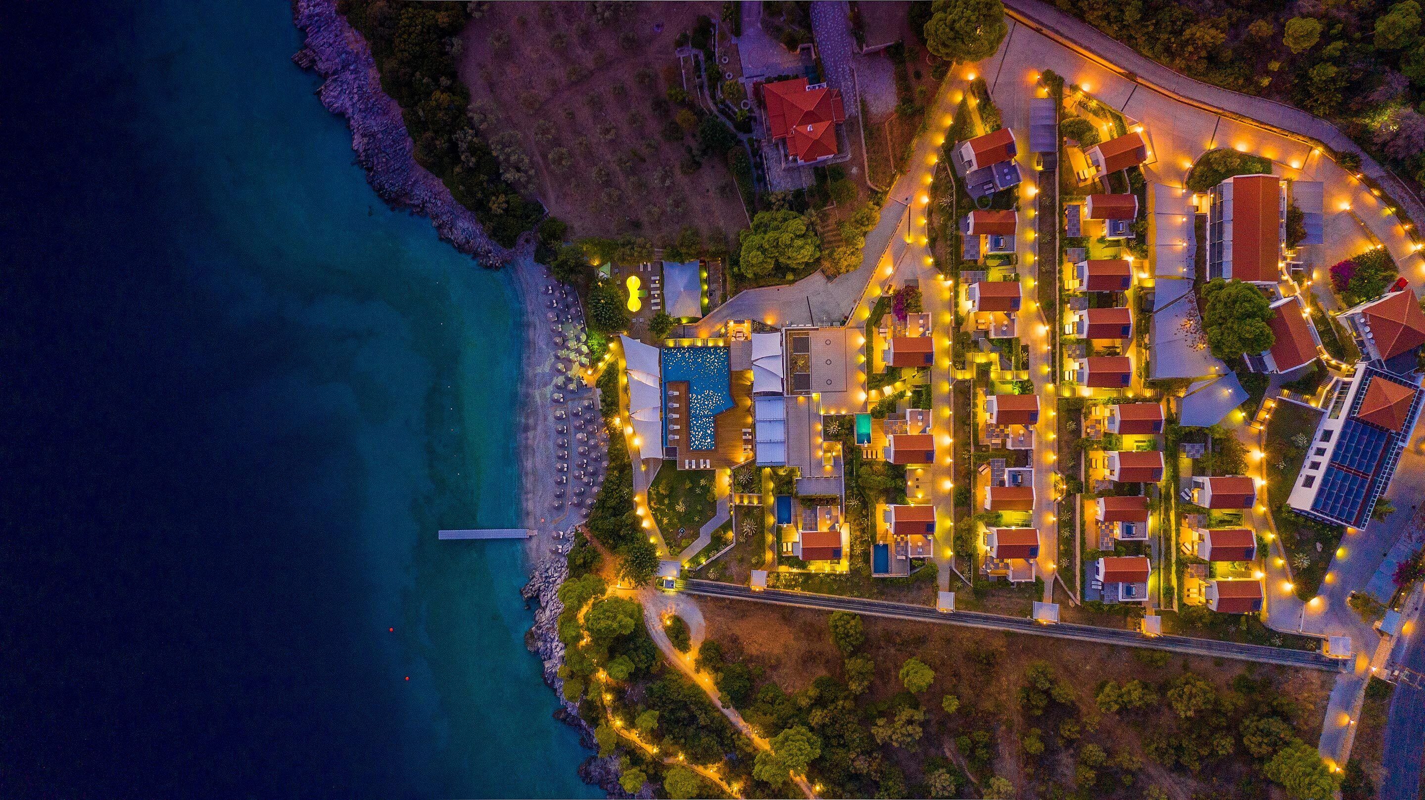 An aerial view of a coastal resort with multiple buildings, a swimming pool, and a pier.