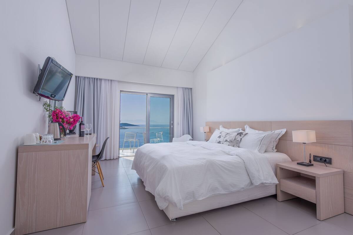 A modern hotel room with a bed, bedside table, TV, and a desk with a chair.