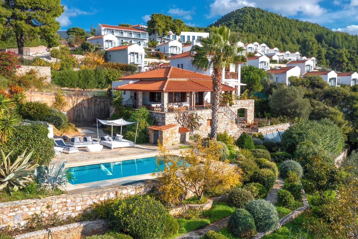 A hillside villa with a swimming pool, stone walls, and lush greenery.