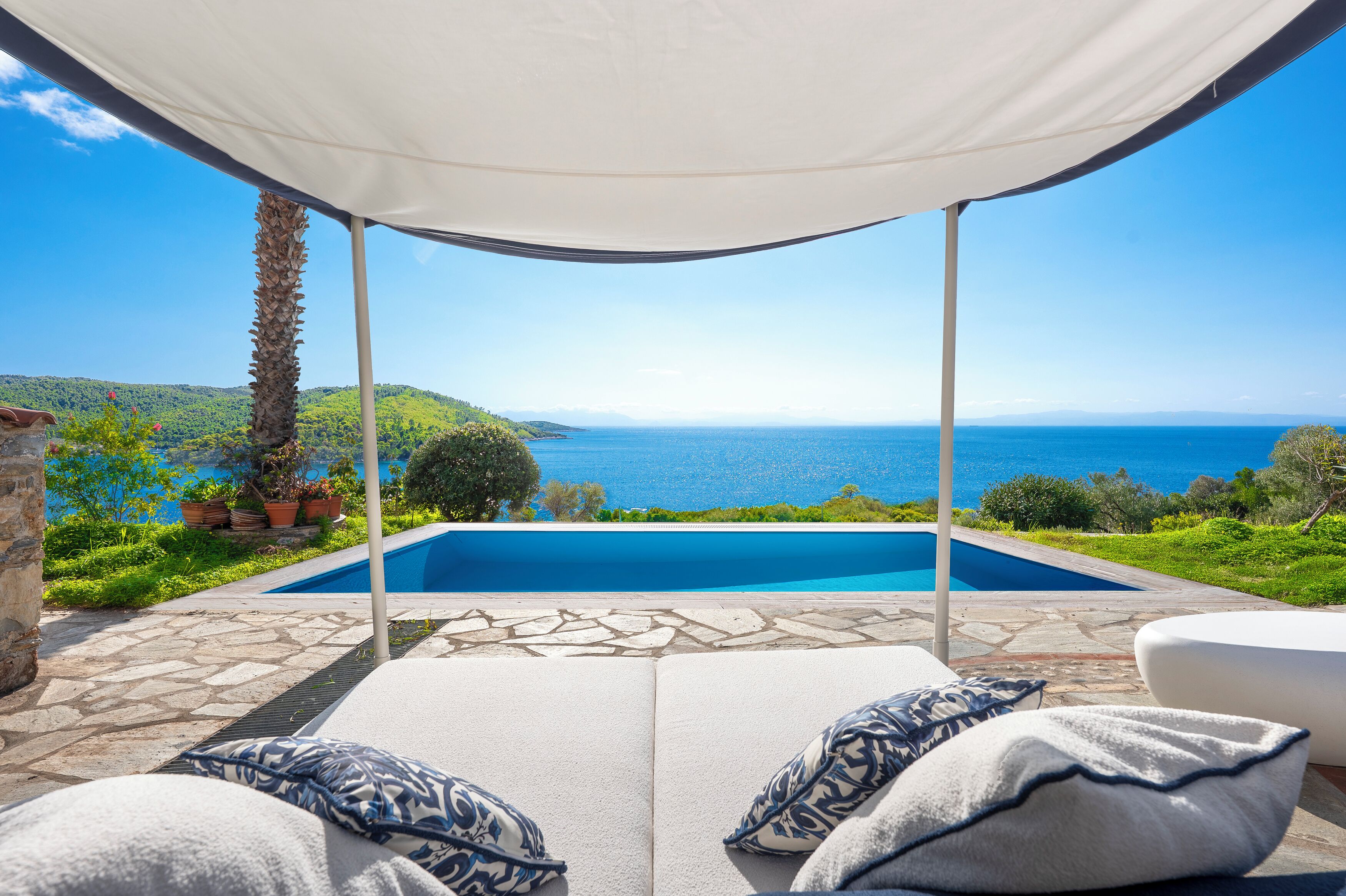 Un espace aménagé au bord de la piscine avec vue sur la mer, un coin salon abrité et un chemin en pierre.