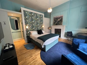 A bedroom with a bed, a mirror, a fireplace, and a blue sofa.
