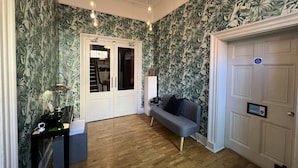 A room with a wooden floor, a grey sofa, a white door, and a wall with a tropical leaf pattern. - Manorhaus Ruthin (Ruthin)