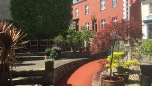 A red pathway in a courtyard with potted plants and a building with a clock tower. - Manorhaus Ruthin (Ruthin)