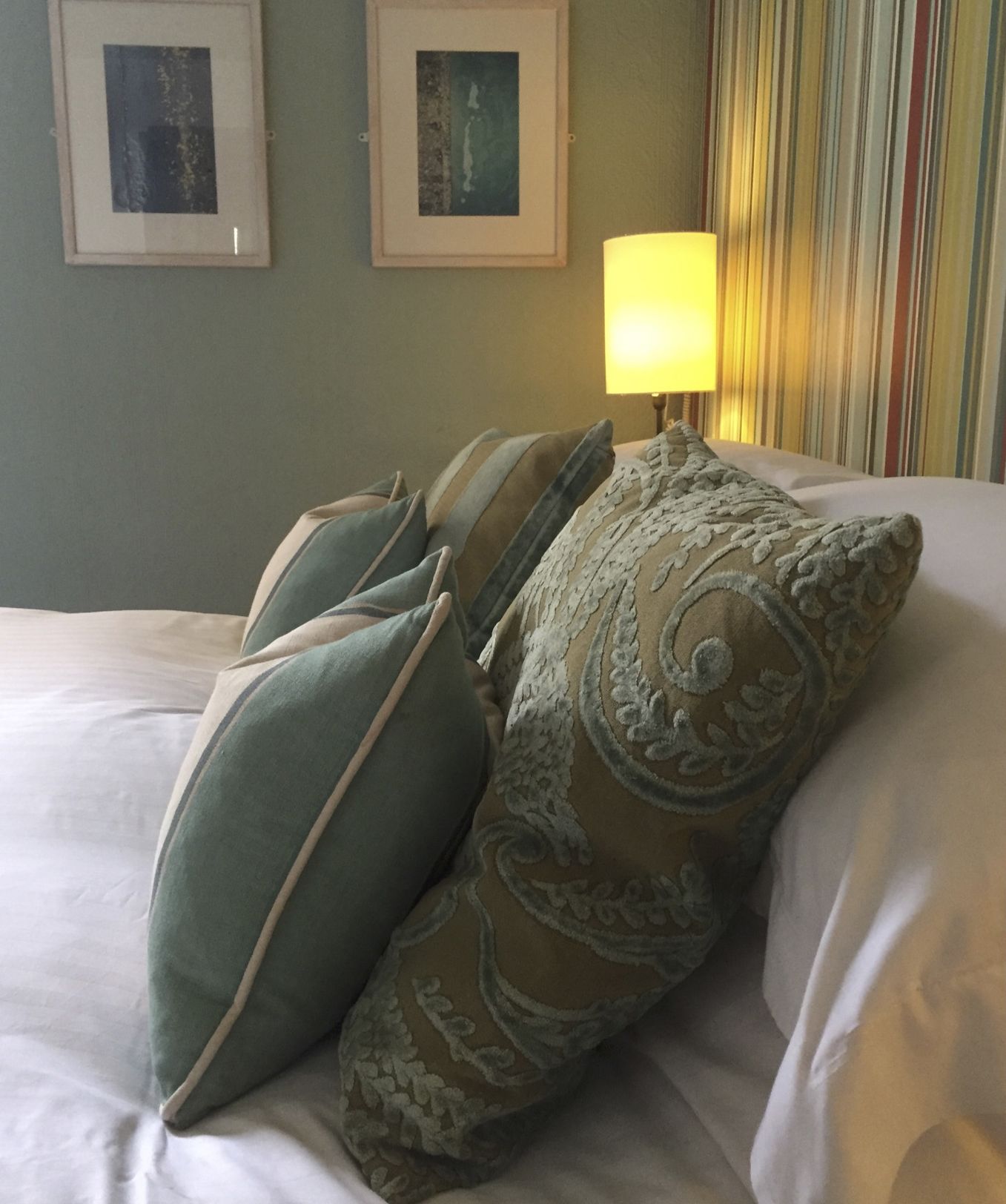 Una cama con varias almohadas y una lámpara en una mesita de noche.