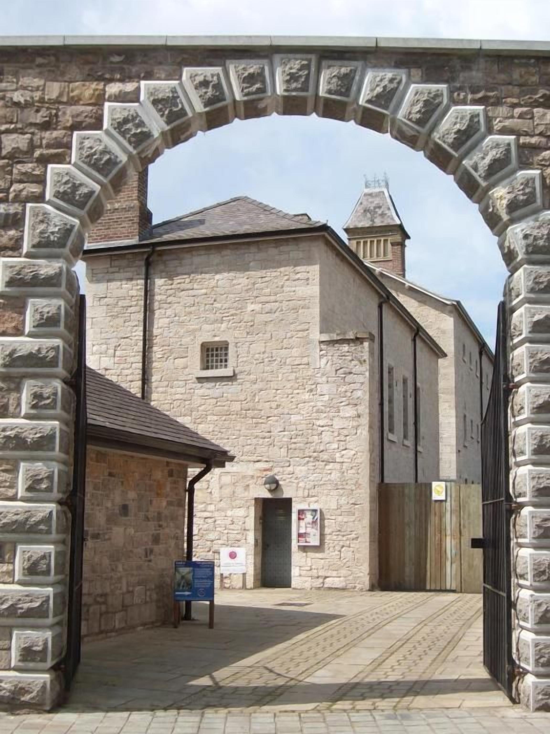 A stone building with a large arched entrance, a small attached structure, and a sign on the ground.