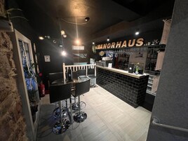 Área de bar com balcão preto, banquetas e placa com a inscrição 'MANORHAUS'.