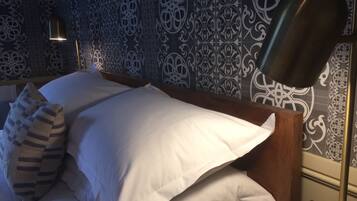 A neatly made bed with white linens, a striped pillow, and a modern floor lamp.