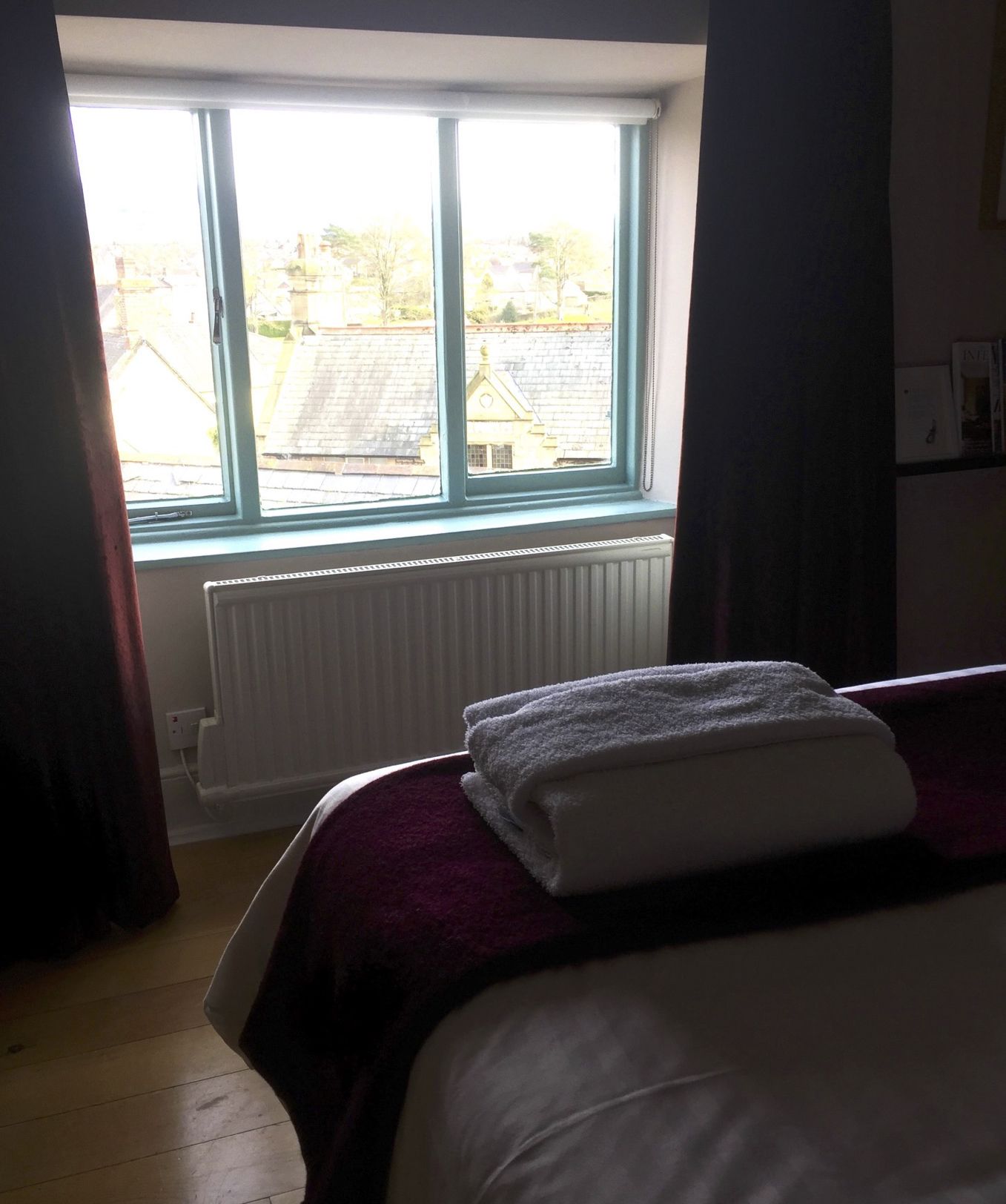 Een hotelkamer met een groot raam, een bed met een wit en paars dekbed, en een radiator onder het raam.