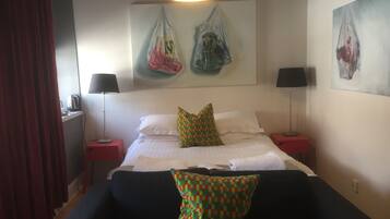 A hotel room with a bed, two nightstands, a black sofa, and a red curtain.