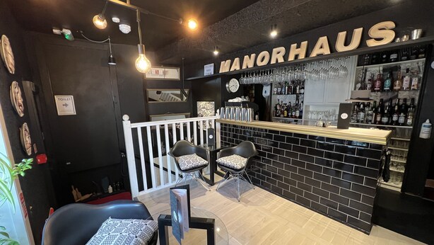 A bar area with a black and white checkered bar stool, a white railing, and a sign that reads "MANORHAUS". - Manorhaus Ruthin (Ruthin)