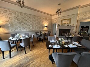 A dining area with round tables, chairs, and a fireplace.