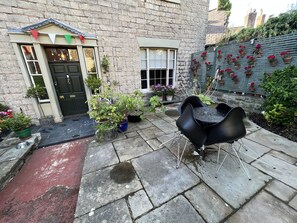 A stone building with a black door, potted plants, and a patio with black chairs.