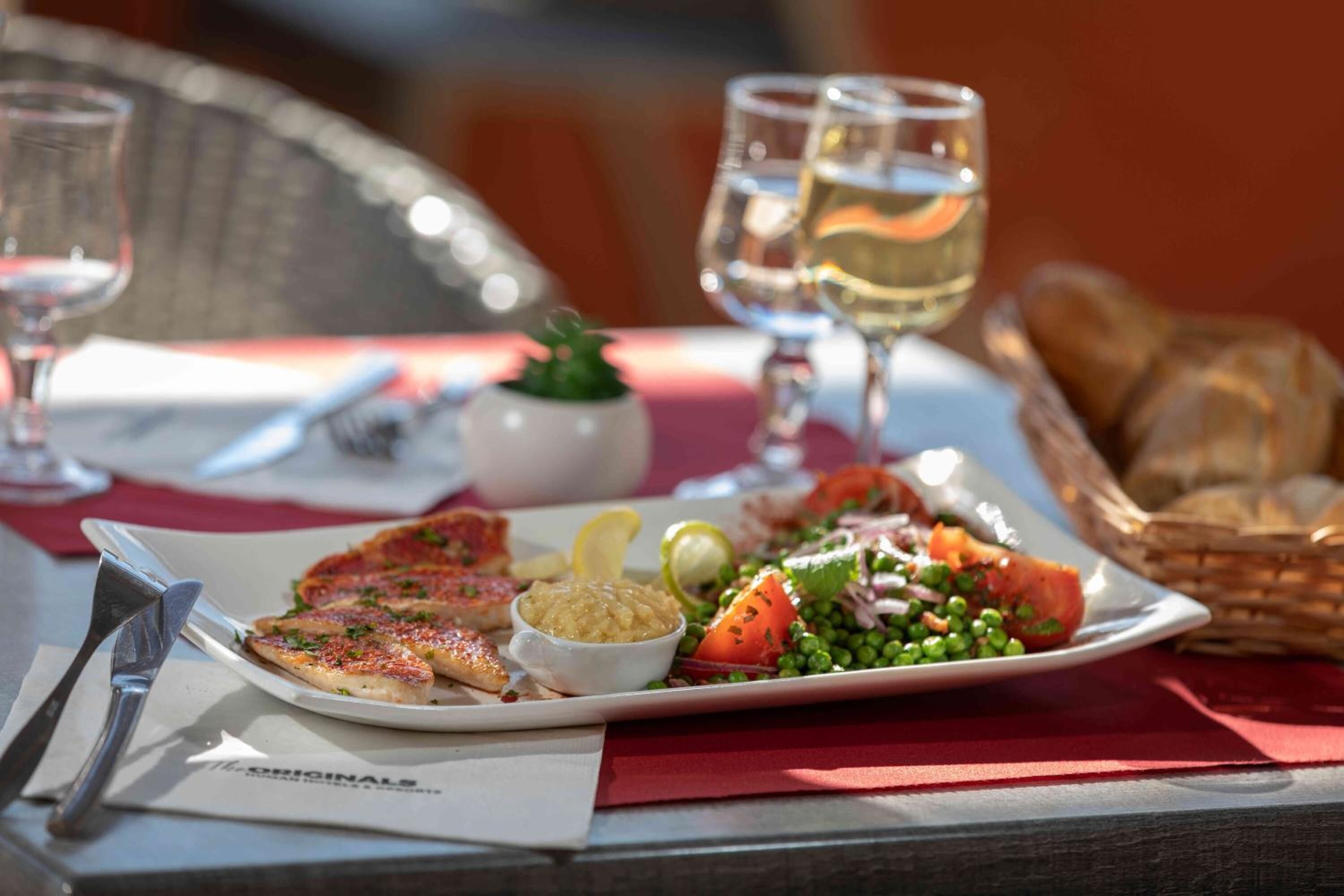 Un repas composé de poisson, de salade et de pain, servi sur une table avec une serviette rouge et deux verres de vin blanc.