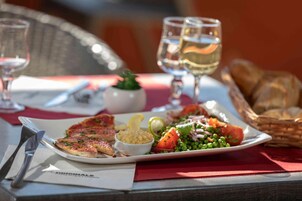 Plato con pescado, ensalada y pan sobre una mesa con servilleta roja y dos copas de vino blanco.