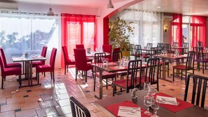 Een restaurant met rode stoelen en tafels, grote ramen met rode gordijnen en een betegelde vloer.