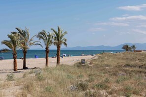 Una playa con palmeras, orilla de arena y vista despejada del mar y montañas distantes.