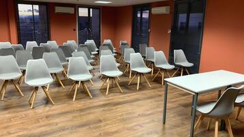 Un salón de conferencias con hileras de sillas blancas, una mesa blanca y suelo de madera.