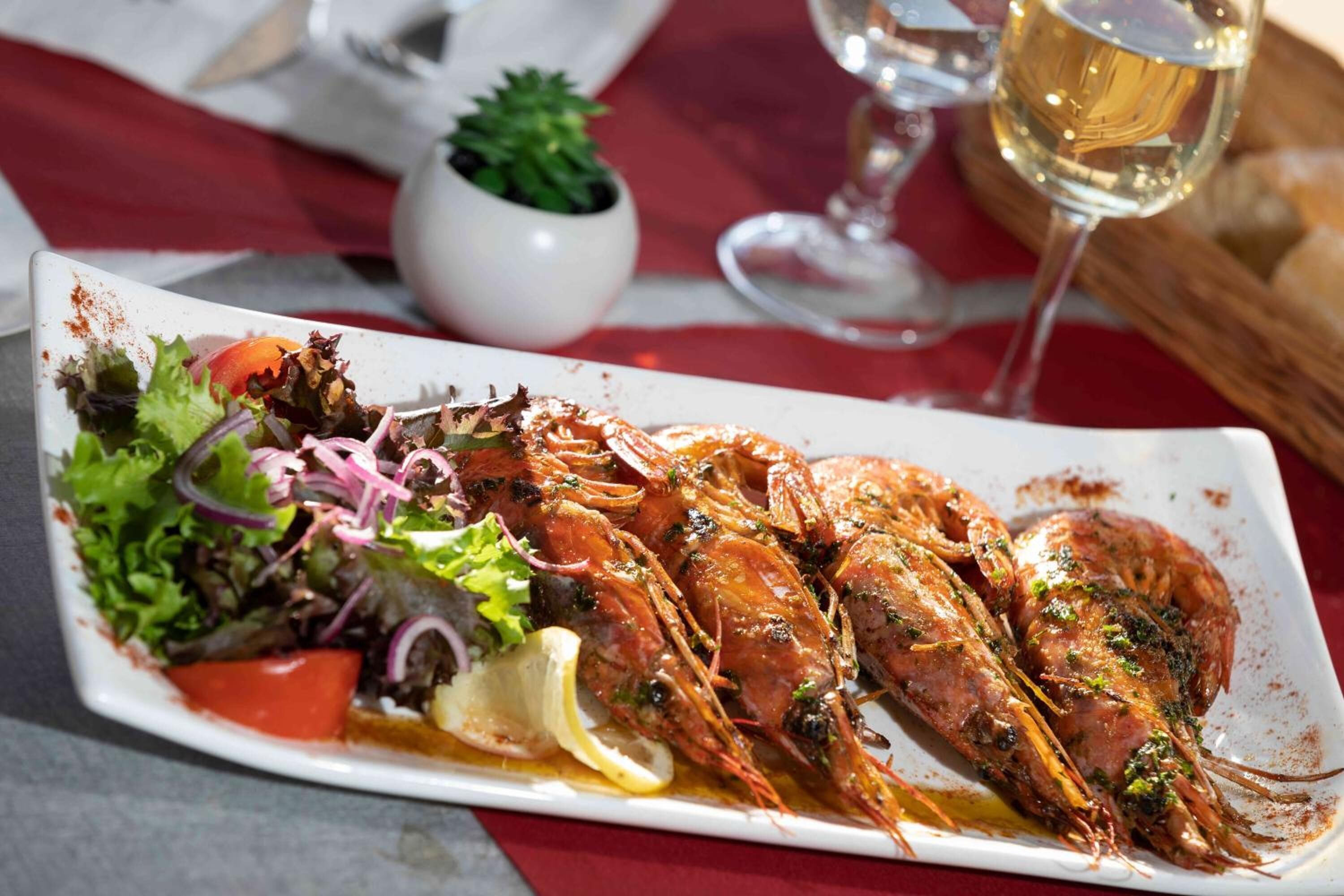 A plate of cooked shrimp with lemon and salad on a white rectangular plate.
