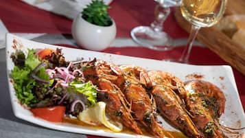 A plate of cooked shrimp with lemon and salad on a white rectangular plate.