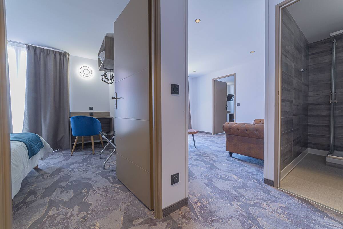 Ein Hotelzimmer mit einem Bett, einem blauen Sessel, einem braunen Sofa und einem Duschbereich.