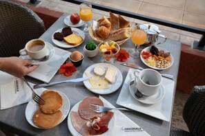Een ontbijttafel met diverse soorten eten, zoals pannenkoeken, kaas, ham en gebak.