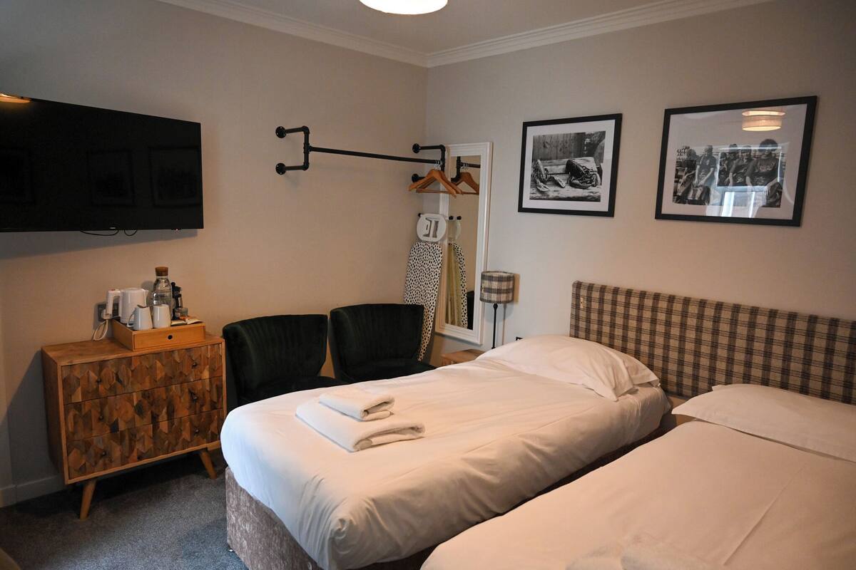 A hotel room with two beds, a wooden dresser, a flat-screen TV, and two framed pictures on the wall.