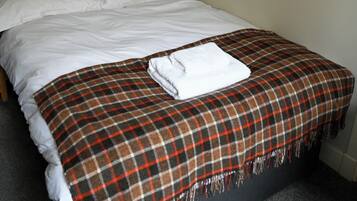 Una cama bien hecha con una colcha escocesa y una toalla blanca doblada, fotografías en blanco y negro en la pared, y un cabecero oscuro.