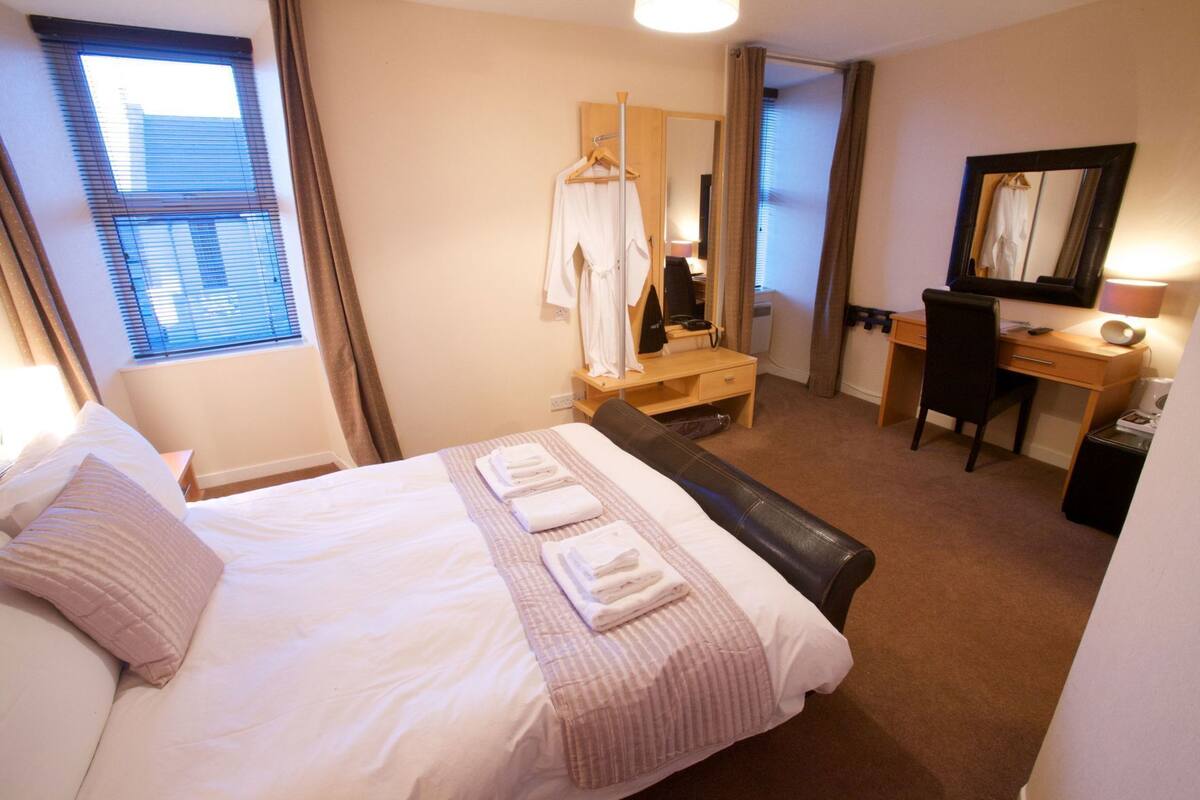 A hotel room with a bed, a desk, a chair, a mirror, and a hanging coat rack.