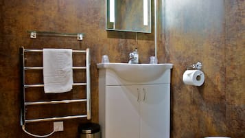 Un baño con suelo de madera, un lavabo blanco, un perchero para toallas, un inodoro y un espejo.