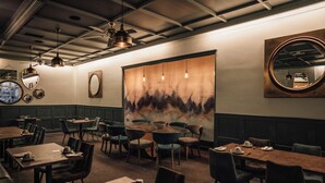 Ein Restaurantinneres mit runden Tischen, Stühlen und einem großen, abstrakten Gemälde an der Wand.