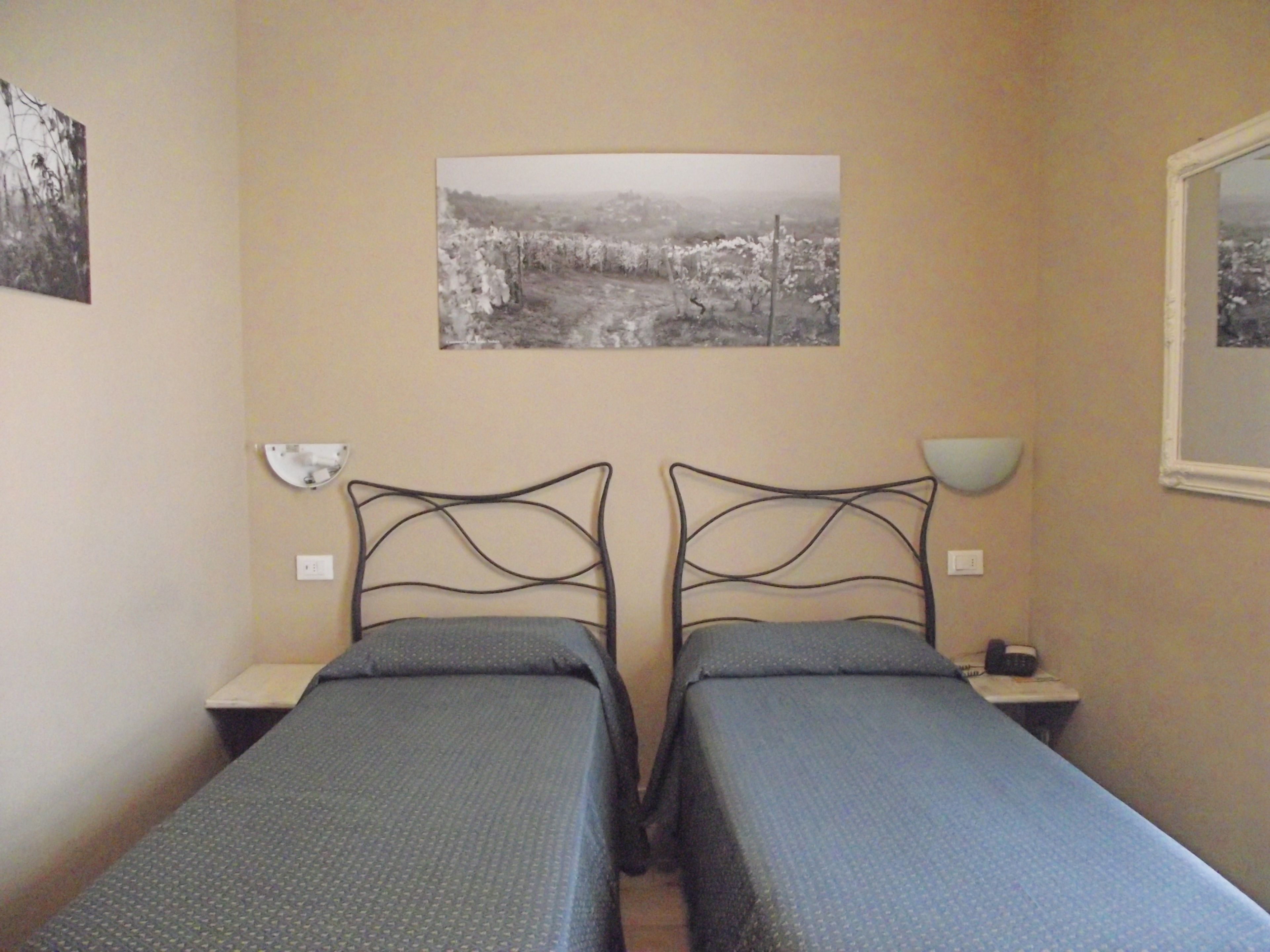 Quarto duplo com duas camas de solteiro, mesa de cabeceira com abajur, um quadro na parede e uma janela.