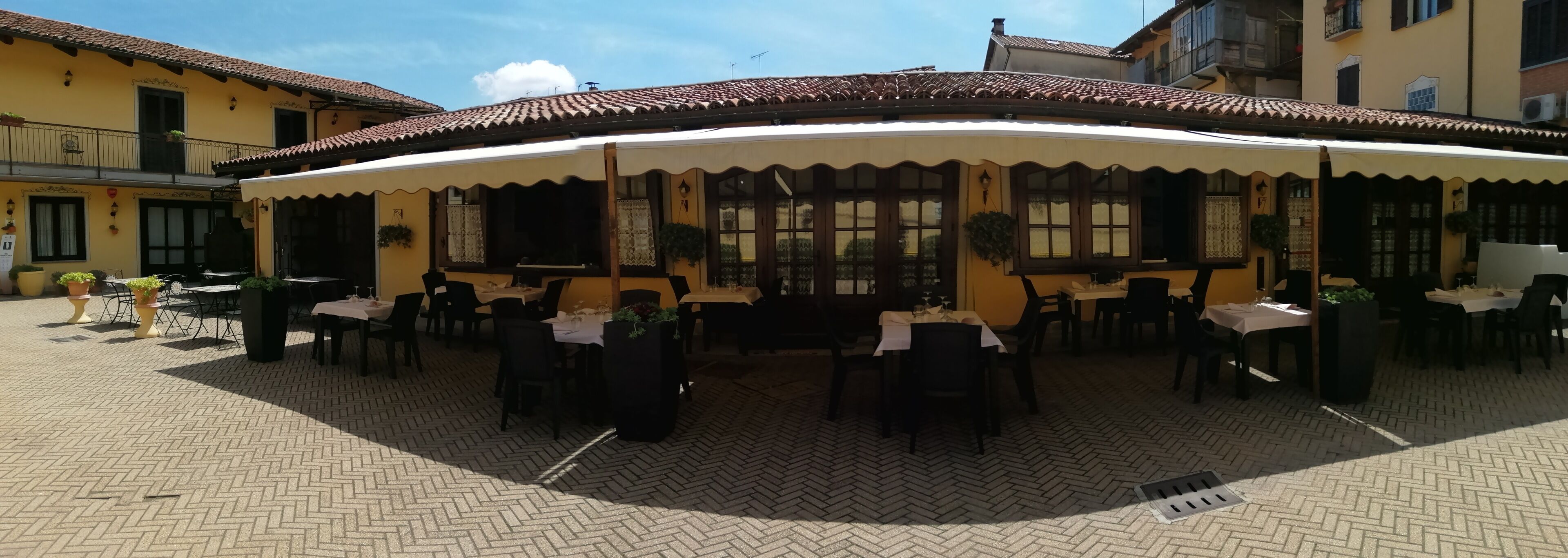An outdoor dining area with tables and chairs, a covered seating area, and a tiled floor.