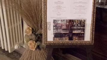 A framed menu stand with a list of items, placed on a wooden floor with a radiator and decorative plants in the background.