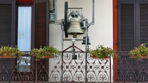 Un orologio montato sulla facciata di un edificio, con ringhiere in metallo decorate e fioriere.