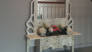 Uno specchio bianco e decorato, con un elegante supporto e un vaso di fiori.
