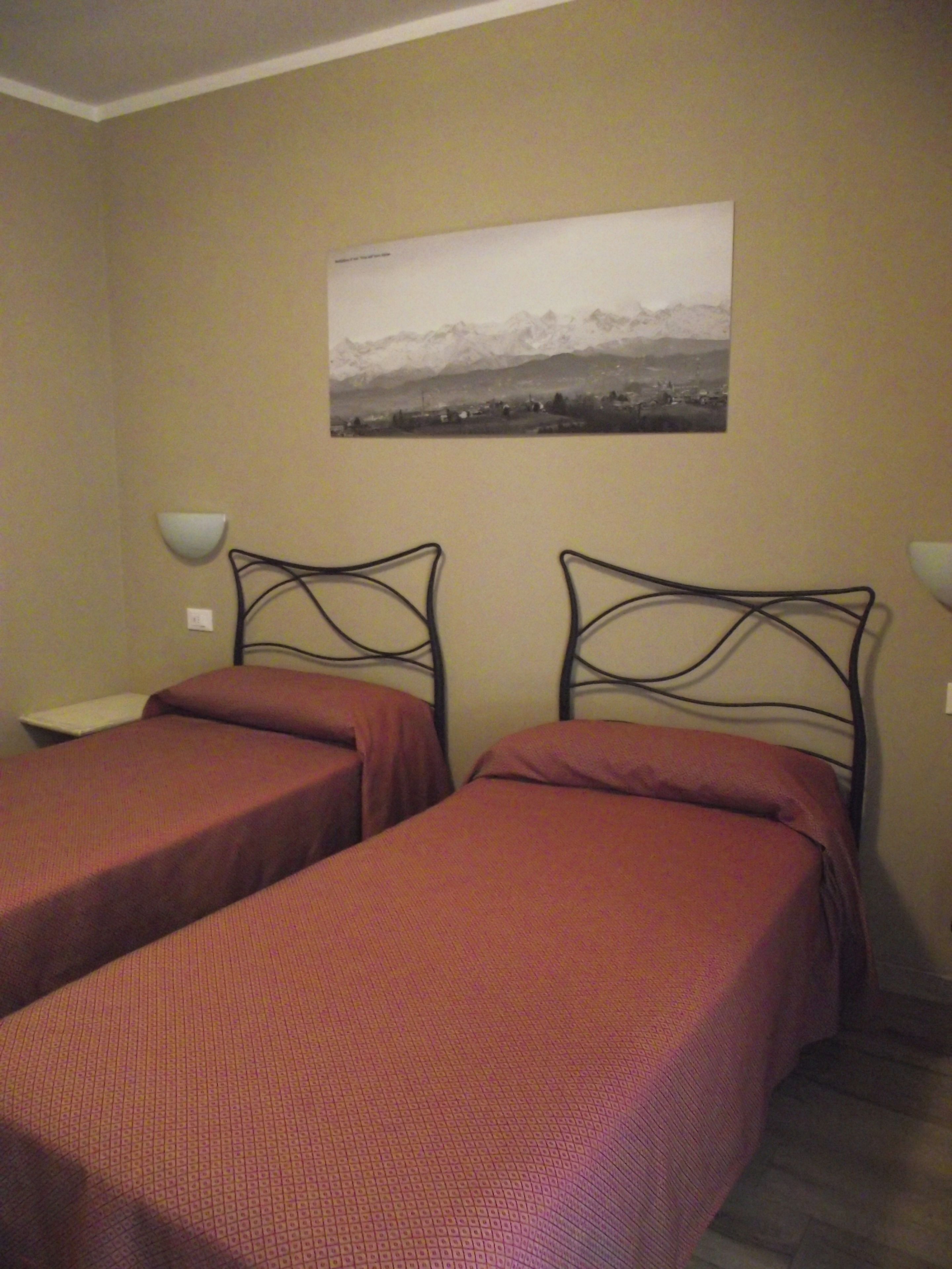 Una habitación con dos camas individuales, un cuadro en la pared y lámparas de noche.