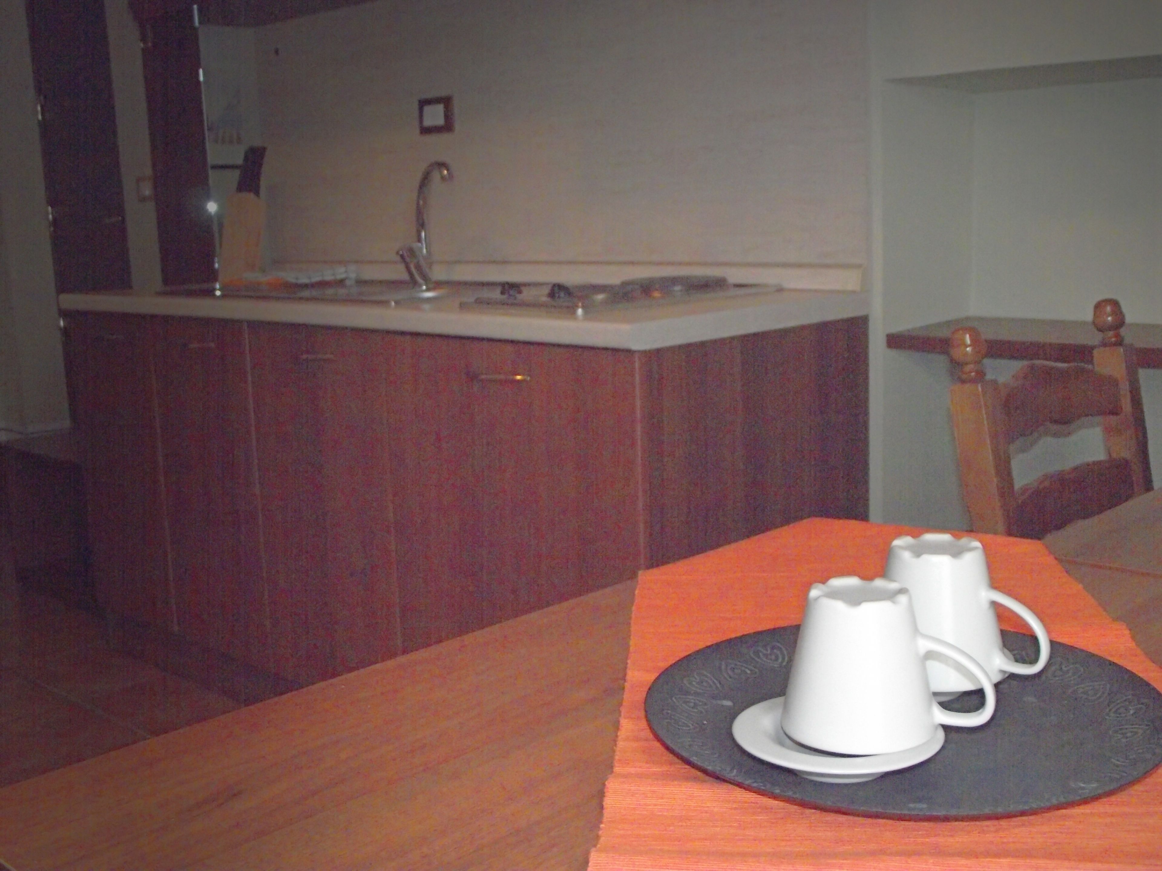 Una cocina con una mesa de madera, dos tazas blancas y un camino de mesa negro.