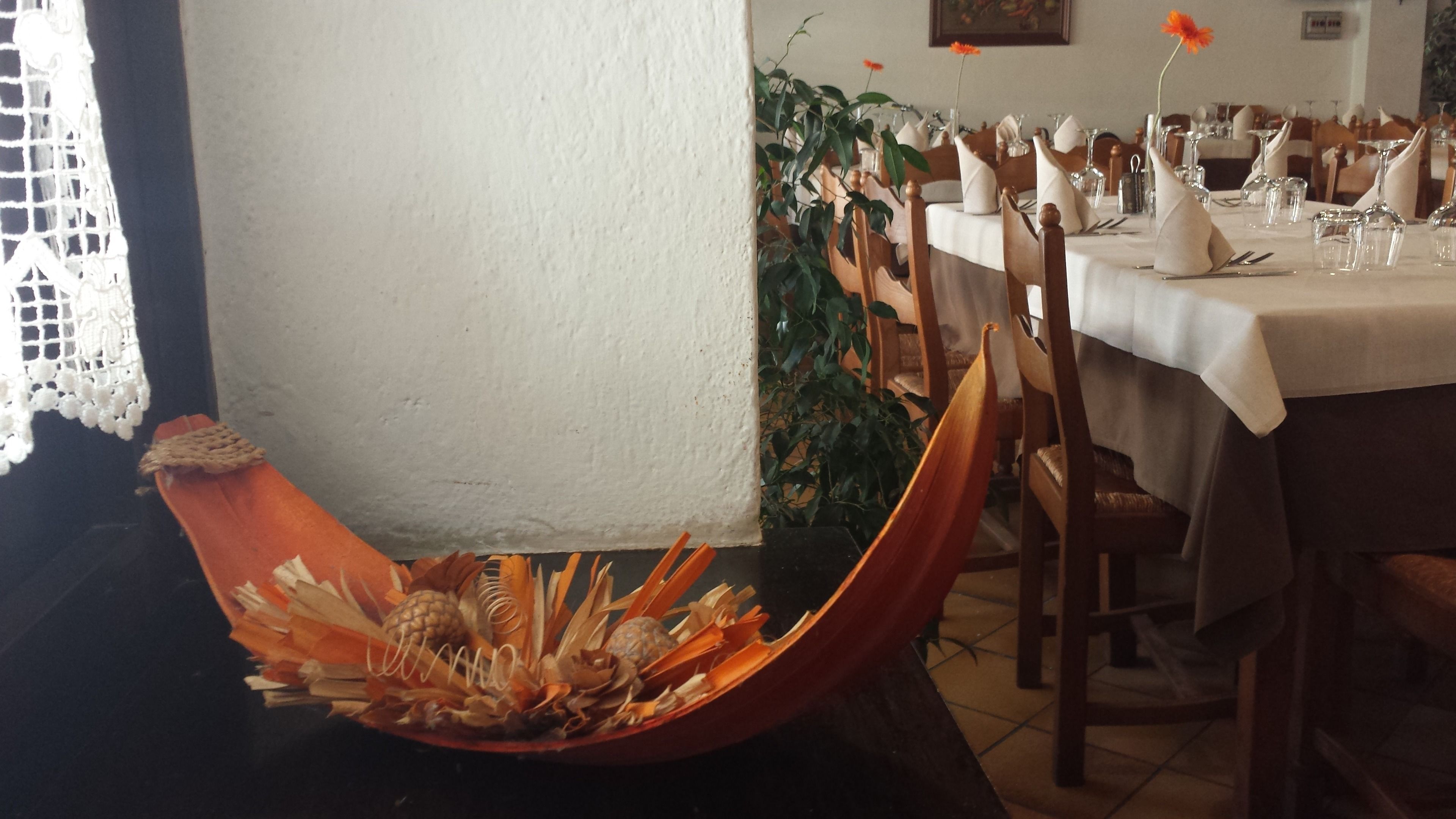 Un espace repas avec une longue table dressée pour accueillir plusieurs convives, des chaises alignées le long de la table et un vase décoratif contenant des éléments naturels, posé sur le sol.