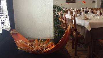 Un espace repas avec une longue table dressée pour accueillir plusieurs convives, des chaises alignées le long de la table et un vase décoratif contenant des éléments naturels, posé sur le sol.