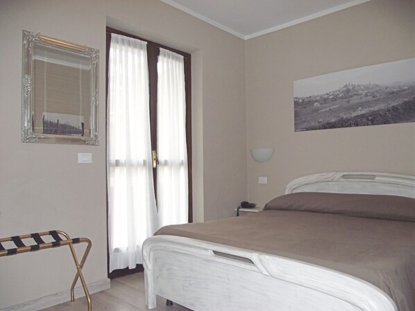 A bedroom with a bed, a bedside table, a lamp, a mirror, and a window with curtains. - Albergo Ciocca (Castelnuovo don Bosco)