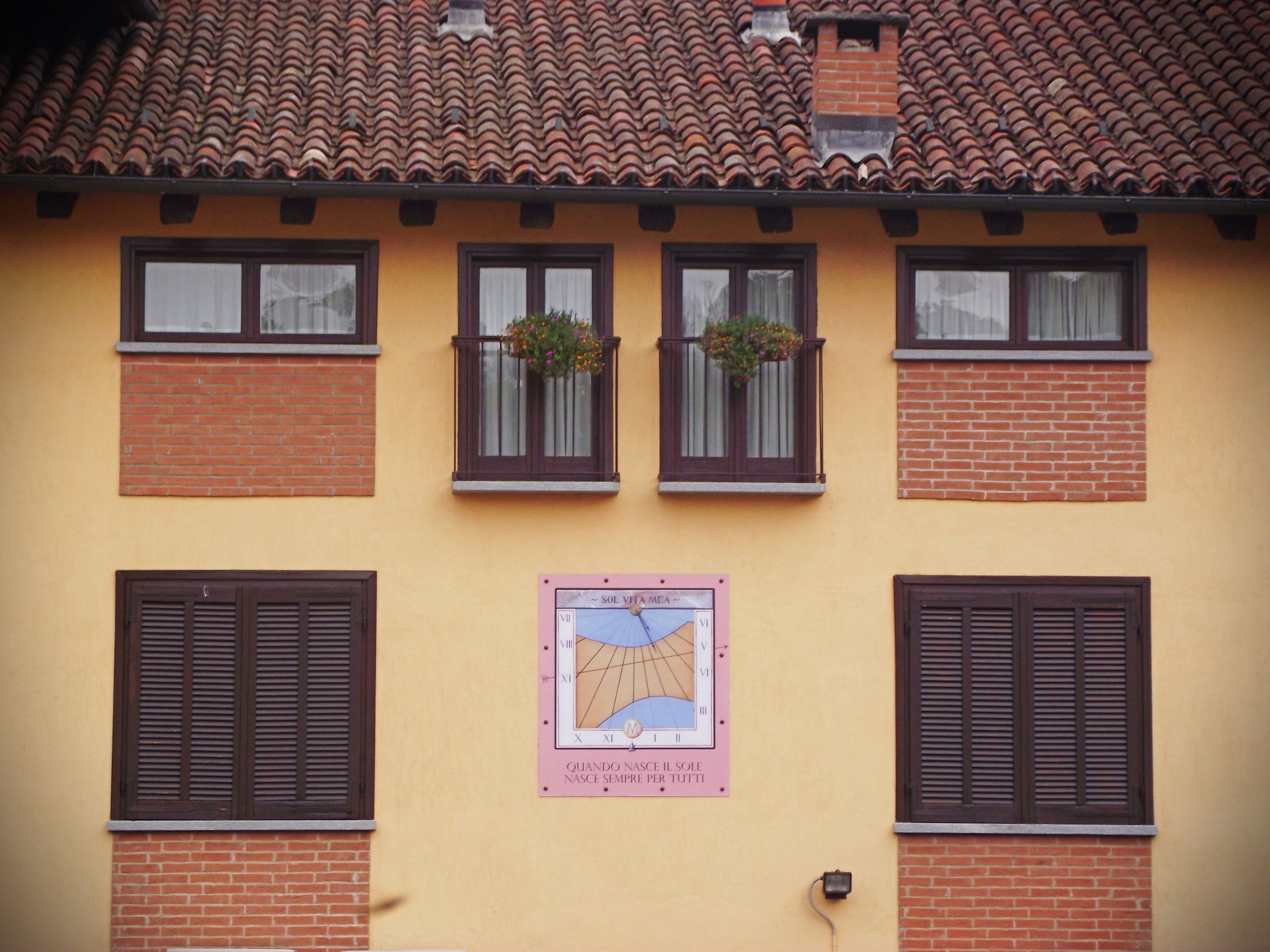 A building with a yellow facade, red-tiled roof, and multiple windows with shutters.