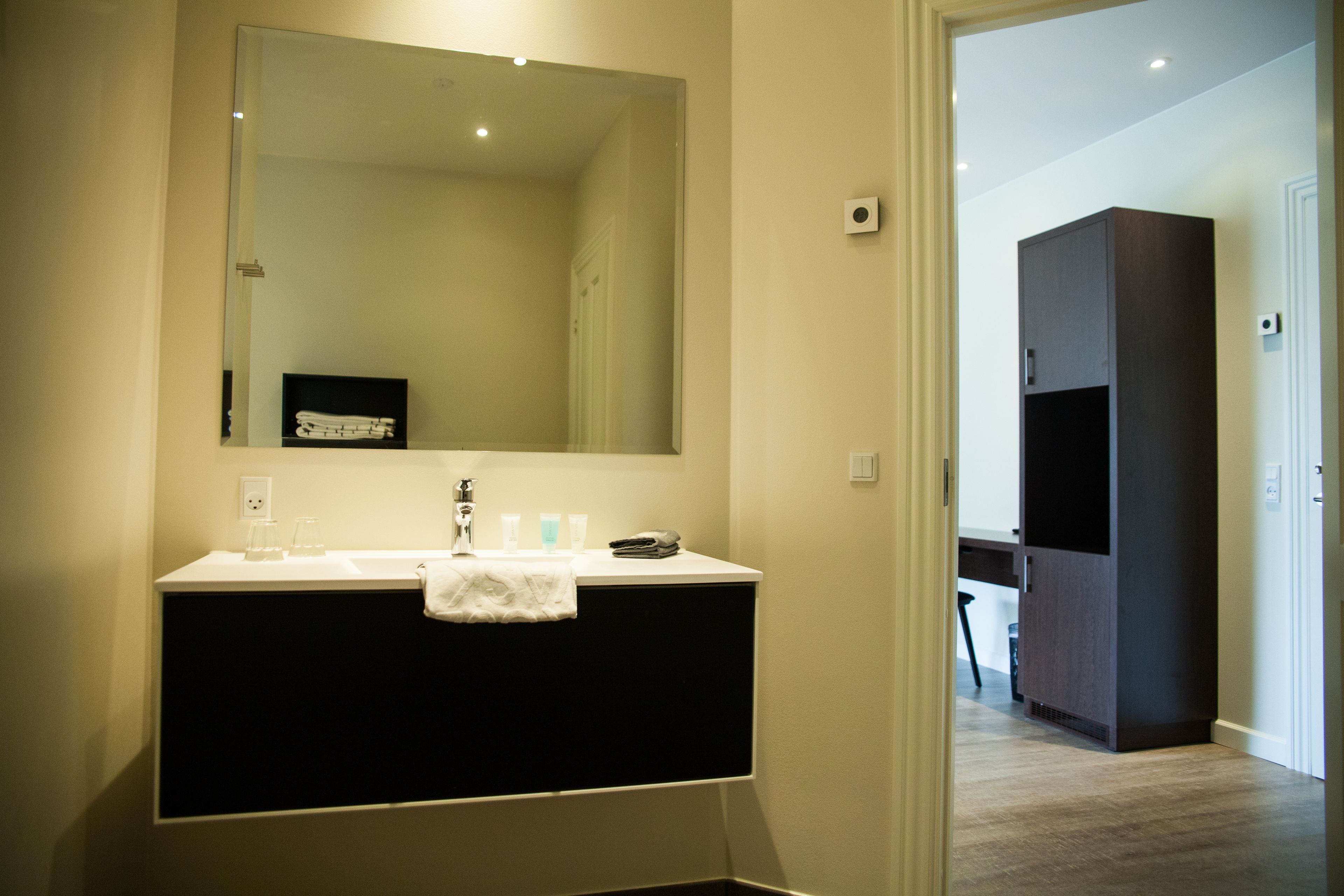 A modern bathroom with a large mirror, a white sink, and a dark vanity.